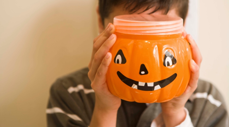 Boy hiding behind jack-o-lantern container